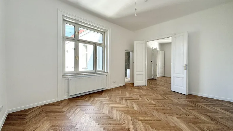 Helles, leeres Zimmer mit Fischgrätparkettboden und hohen Decken, bereit zur individuellen Gestaltung.