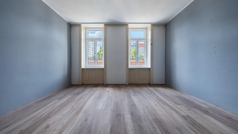 Helles Zimmer mit blaugrauen Wänden und neuem Laminatboden, bereit zur individuellen Gestaltung.