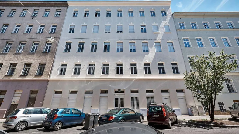Mehrstöckiges Wohngebäude mit vielen Fenstern und parkenden Autos auf der Straße.