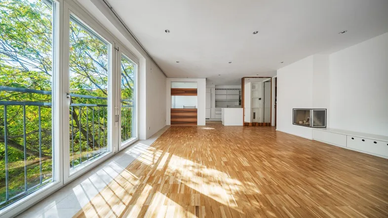 Helles Wohnzimmer mit Parkettboden, großen Fenstern und Zugang zu einem Balkon.