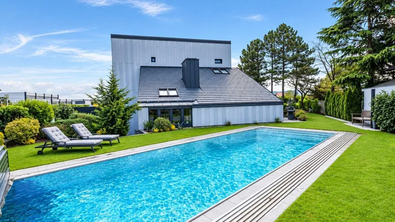 Modernes Haus mit großem Pool und gepflegtem Garten unter blauem Himmel.