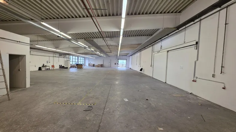 Große, leere Lagerhalle mit Betonboden und sichtbaren Deckenstrukturen, bereit zur Nutzung.