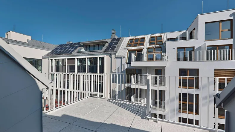 Geräumige Dachterrasse mit Blick auf moderne Gebäude und Solarpaneele unter blauem Himmel.