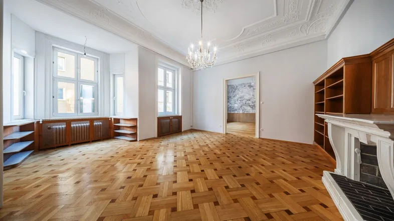 Geräumiges Wohnzimmer mit Fischgrätparkett, Stuckdecke, Kronleuchter und Kamin.