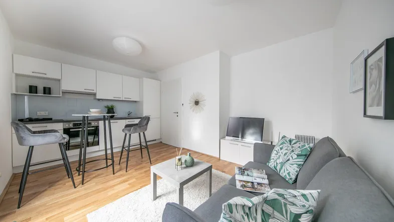 Heller offener Wohnbereich mit integrierter Küche, Parkettboden und modernem Sofa.