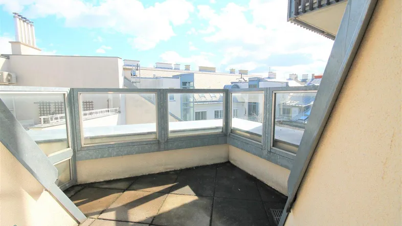 Heller Balkon mit Glasbrüstung und Blick auf die umliegenden Dächer der Stadt.