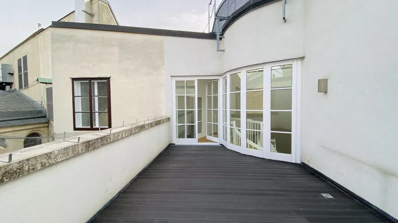 Große Dachterrasse mit dunklem Holzboden und Zugang zu den Innenräumen, umgeben von Stadtgebäuden.