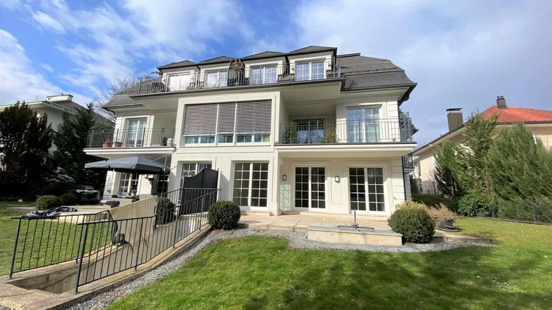Modernes Mehrfamilienhaus mit mehreren Balkonen, Terrassen und einem gepflegten Gartenbereich.