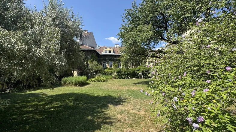 Weitläufiger Garten mit Rasen, blühenden Sträuchern und Blick auf das historische Gebäude.