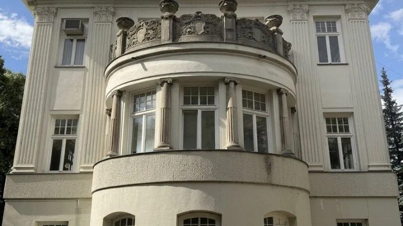 Eindrucksvolle historische Villa mit eleganter Fassade, großen Fenstern und Mansarddach unter blauem Himmel.