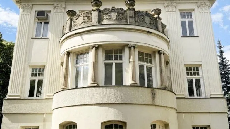 Elegante Stadtvilla mit klassischer Architektur, markantem Mansarddach und einem verzierten Balkon.