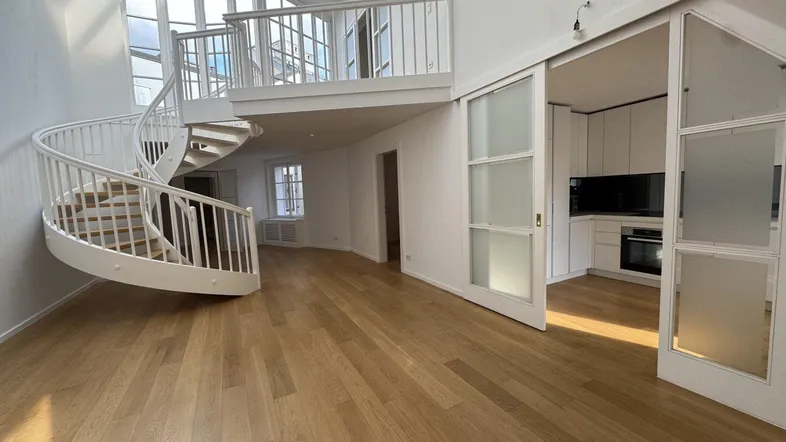 Helles, offenes Wohnzimmer mit eleganter Wendeltreppe, hohen Decken und Zugang zu einer modernen Küche.