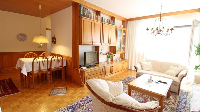 Heller Wohn- und Essbereich mit Parkettboden, Holzmöbeln und Zugang zum Balkon.