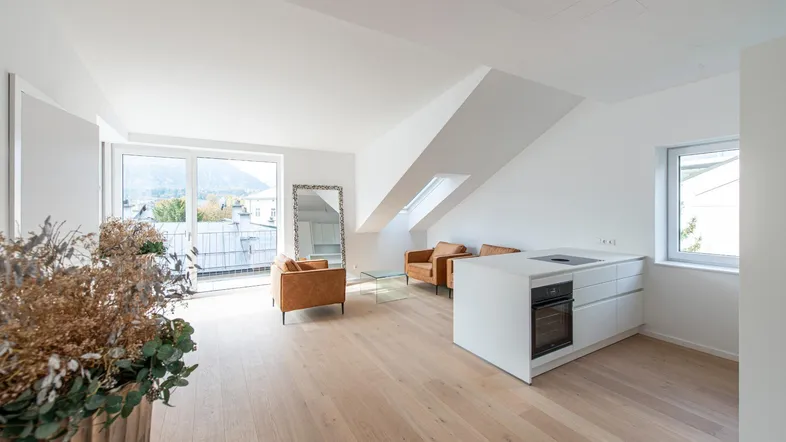 Helles, offenes Wohnzimmer mit integrierter Küche, Holzboden und Zugang zum Balkon mit Bergblick.