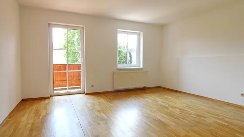 Helles Zimmer mit Parkettboden und Zugang zu einem kleinen Balkon, ideal als Wohn- oder Schlafzimmer.