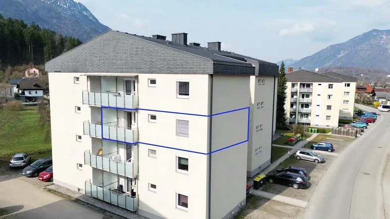 Luftaufnahme eines Mehrfamilienhauses mit Balkonen und Bergblick in ländlicher Umgebung.