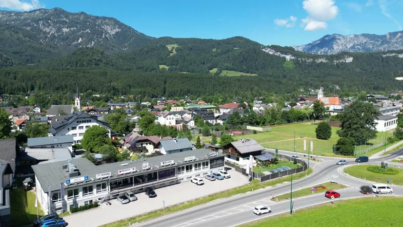 Luftaufnahme einer ländlichen Gegend mit Bergen, Häusern und einer Straße unter blauem Himmel.