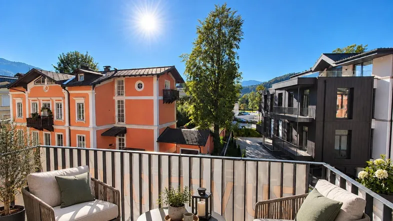 Sonniger Balkon mit bequemen Sitzmöbeln und Blick auf die umliegenden Gebäude und Berge.