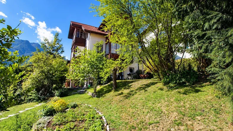 Gepflegter Gartenbereich mit Rasenfläche und Blick auf das Haus sowie die umliegenden Berge.