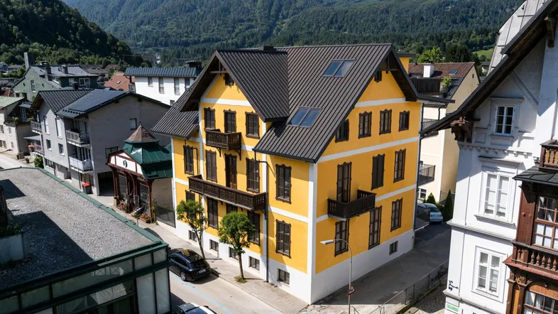 Historisches Gebäude mit gelber Fassade, dunklem Dach und traditionellen Holzbalkonen in bergiger Umgebung.