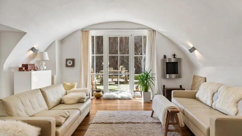 Helles Wohnzimmer mit gewölbter Decke, Holzboden und Zugang zu einem charmanten Gartenbereich.