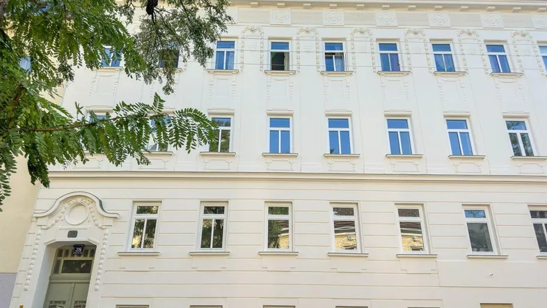 Klassische Fassade eines gepflegten Mehrfamilienhauses mit vielen Fenstern und dekorativen Elementen.