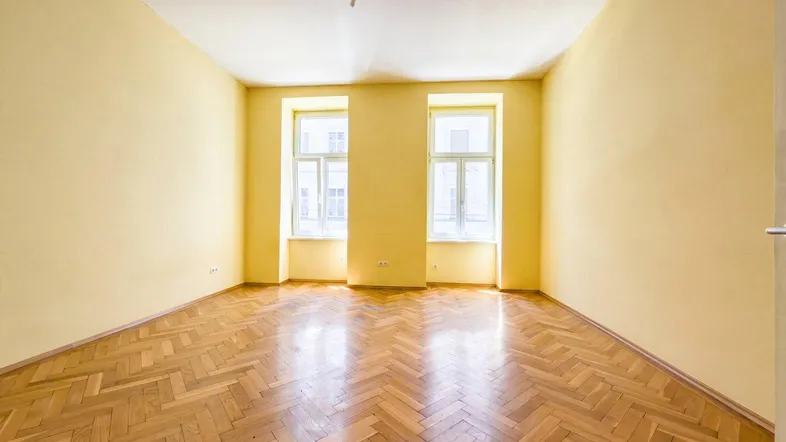 Helles Zimmer mit gelben Wänden und klassischem Fischgrätparkettboden.