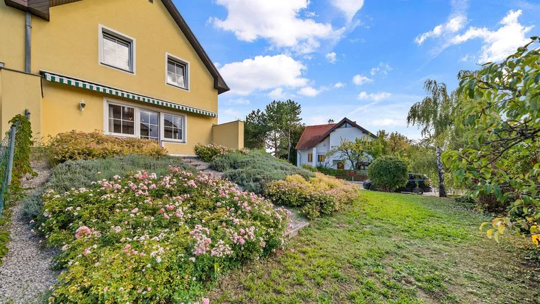 Gelbes Haus mit gepflegtem Garten, blühenden Rosen und einer Markise über der Terrasse.