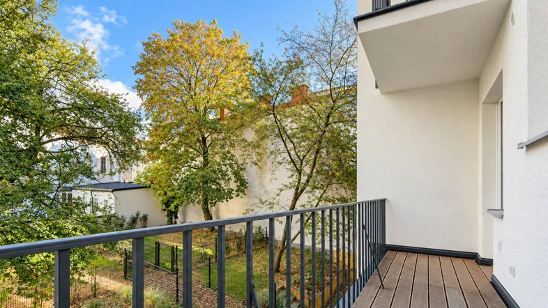 Balkon mit Holzboden und Blick auf den grünen Innenhof, umgeben von Bäumen.