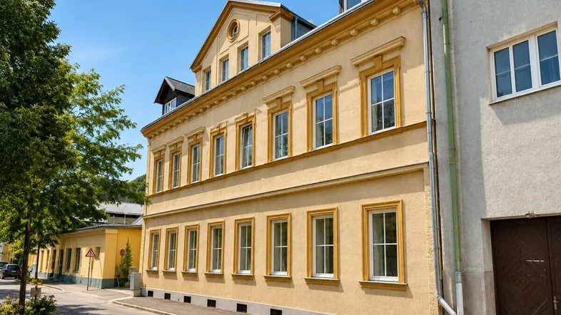 Historisches Gebäude mit gelber Fassade und vielen Fenstern an einer ruhigen Straße gelegen.
