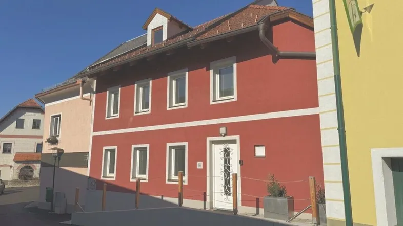 Rotes Gebäude mit weißen Fenstern und einer Rampe zum Eingangsbereich unter blauem Himmel.