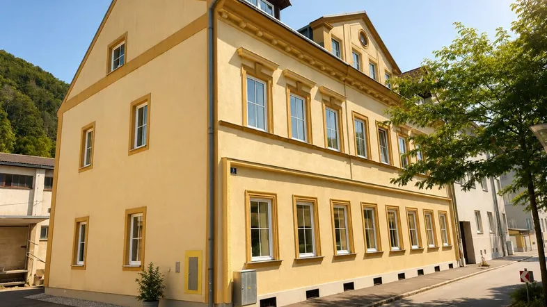 Gelbe Fassade eines Mehrfamilienhauses mit vielen Fenstern und traditionellen Details unter blauem Himmel.