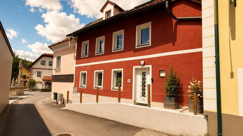 Rotes Wohnhaus mit weißer Eingangstür und Rampe an einer ruhigen Straße gelegen.