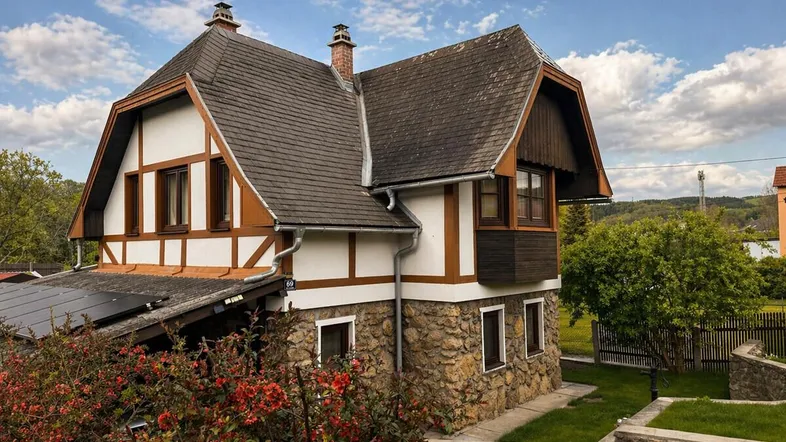 Traditionelles Haus mit Steinfassade, Mansarddach und Photovoltaikanlage unter blauem Himmel.