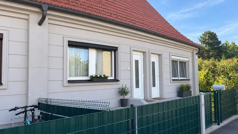 Moderne Doppelhaushälfte mit heller Fassade, roten Dachziegeln und kleinen Vorgärten.