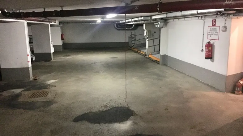 Geräumige Tiefgarage mit mehreren Stellplätzen, sichtbaren Versorgungsleitungen und Brandschutzvorrichtungen.