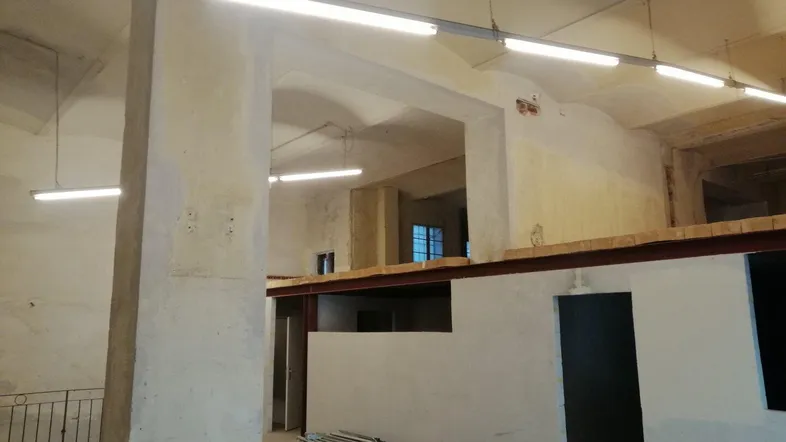 Großer, unfertiger Innenraum mit hohen Decken, Betonpfeilern und sichtbaren Leuchtstoffröhren.