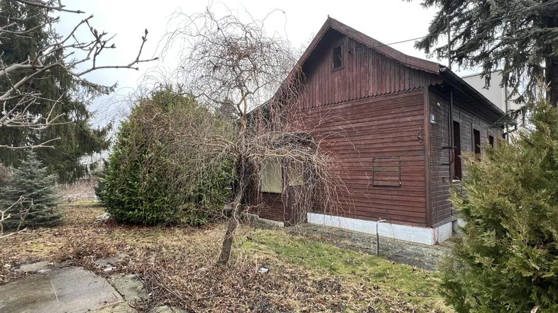 Altes Holzhaus mit Satteldach und verwildertem Garten in ländlicher Umgebung.
