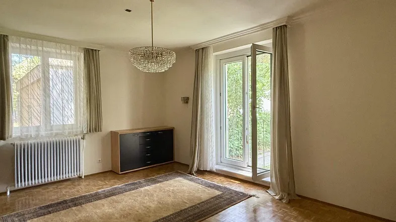Helles Wohnzimmer mit Parkettboden, Kronleuchter und Zugang zu einem Balkon oder einer Terrasse.