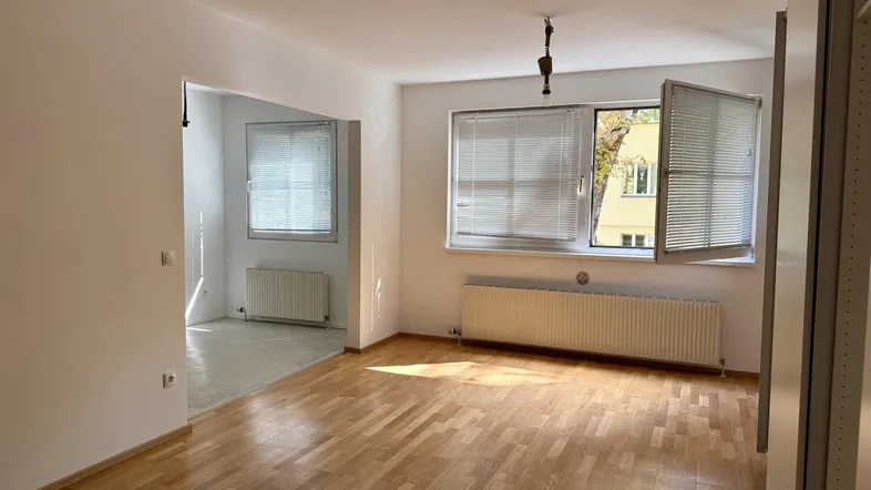 Helles Zimmer mit Parkettboden, weißen Wänden und zwei Fenstern, die viel Tageslicht hereinlassen.