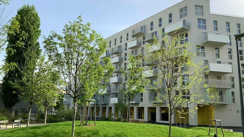 Modernes Wohngebäude mit vielen Balkonen und einer gepflegten Grünfläche im Vordergrund.