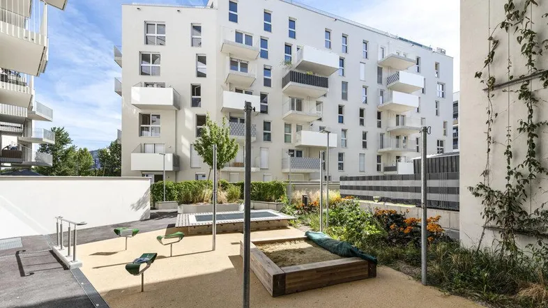 Moderner Wohnkomplex mit weißer Fassade und einem gemeinschaftlichen Spielplatz im Außenbereich.