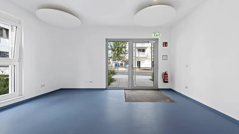Heller Eingangsbereich mit blauen Vinylböden, großen Fenstern und einer Glastür, die nach draußen führt.
