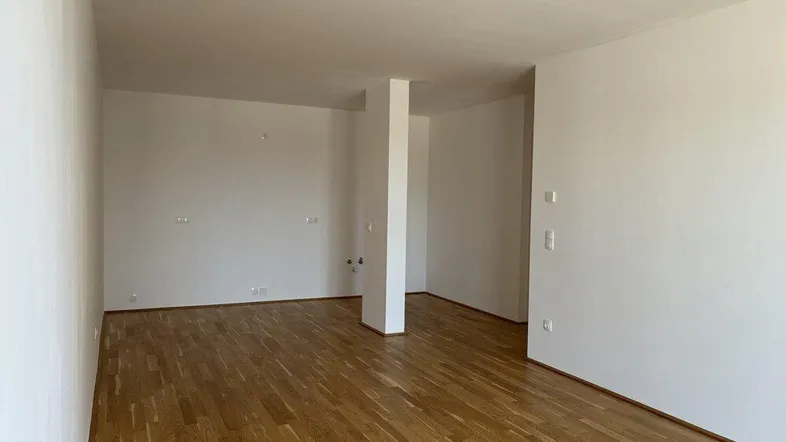 Heller, leerer Wohnbereich mit modernem Parkettboden und weißen Wänden.