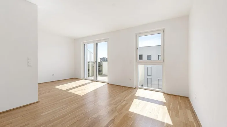 Helles Zimmer mit Holzboden und Zugang zu einem Balkon, durchflutet von natürlichem Sonnenlicht.