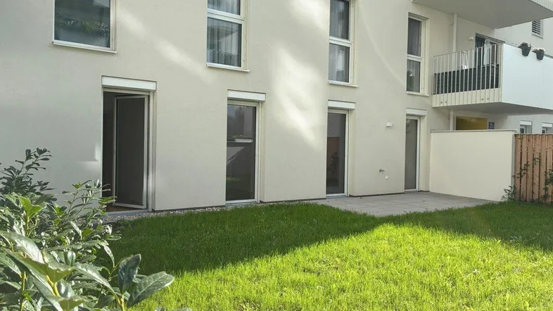 Erdgeschosswohnung mit privater Terrasse und kleinem Gartenbereich vor der modernen Fassade.