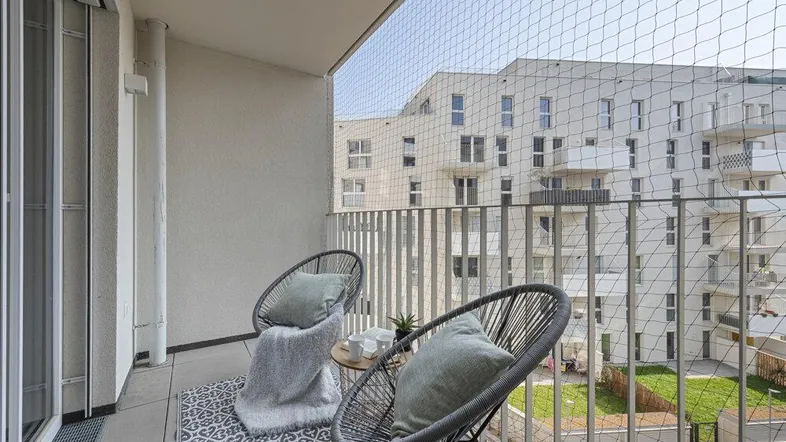 Gemütlicher Balkon mit Sitzgelegenheiten und Blick auf moderne Wohngebäude.