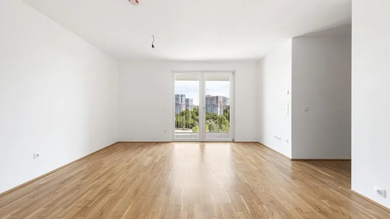 Helles, leeres Zimmer mit Parkettboden und Zugang zu einem Balkon, bietet einen Blick ins Grüne.