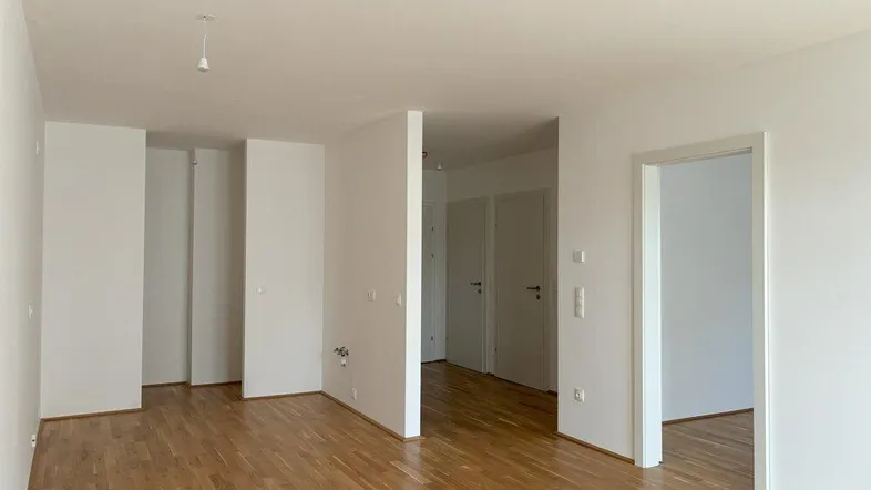 Heller, leerer Wohnbereich mit Parkettboden und weißen Wänden, bereit für die Einrichtung.