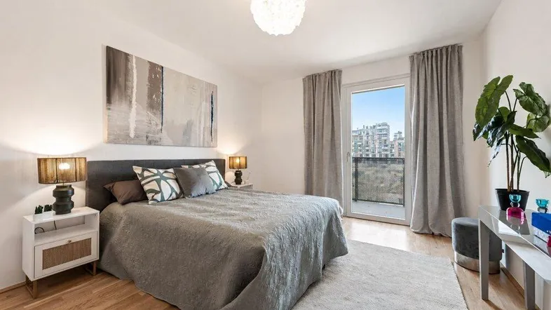 Helles Schlafzimmer mit Holzboden, Zugang zum Balkon und moderner Einrichtung.
